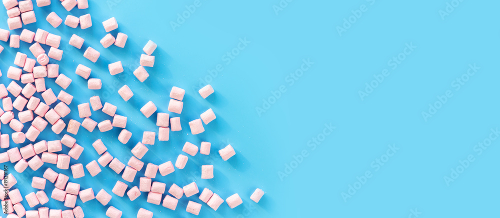 Marshmallows on blue background with copyspace. Flat lay or top view. Background or texture of colorful mini marshmallows. Winter food background concept.