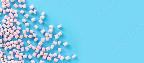 Marshmallows on blue background with copyspace. Flat lay or top view. Background or texture of colorful mini marshmallows. Winter food background concept.