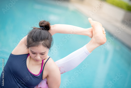 Beautiful young Asian happy woman doing yoga exercise near swimming pool. Healthy lifestyle and good wellness concepts