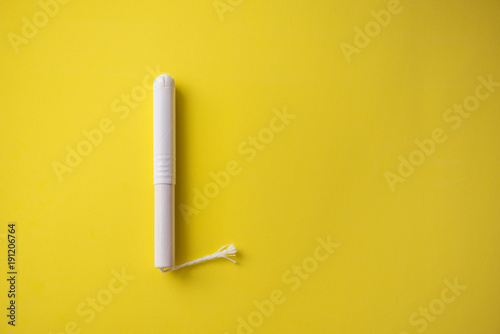 Feminine tampon with paper applicator on yellow background photo