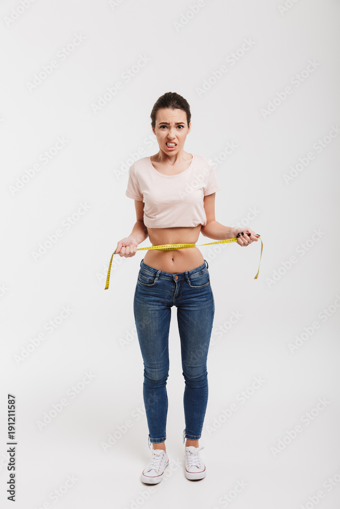 disappointed young woman measuring her waist isolated on white disappointed young woman measuring her waist isolated on white