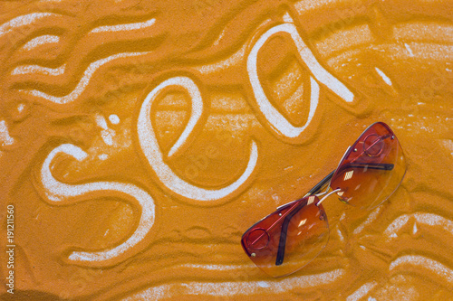 Sea inscription on an orange colored sand with waves and sunglasses, top view, flat lay photo