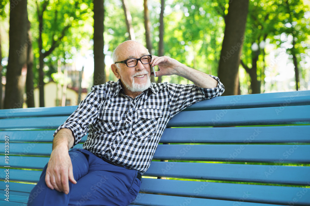 Obraz premium Smiling senior man in casual talking on mobile outdoors