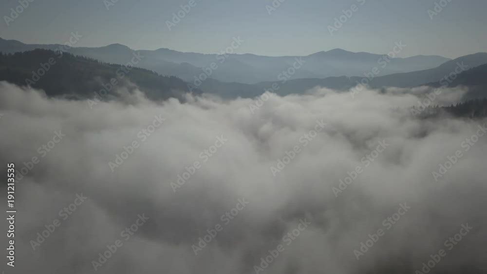 Flying over fog and clouds in Carpathians mountains near by Dzembronya village at sunny day, Ukraine