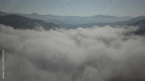 Flying over fog and clouds in Carpathians mountains near by Dzembronya village at sunny day, Ukraine