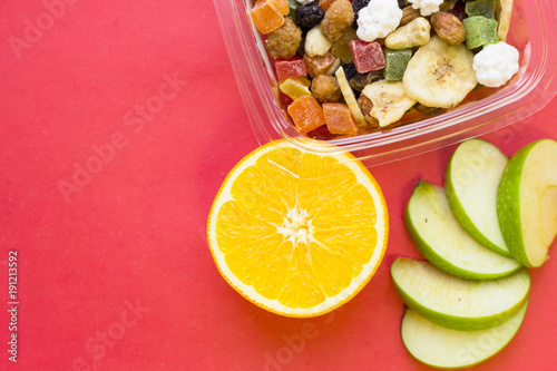 Candied fruit in plastic container, orange, banana and sliced green apple ,rose background, top view