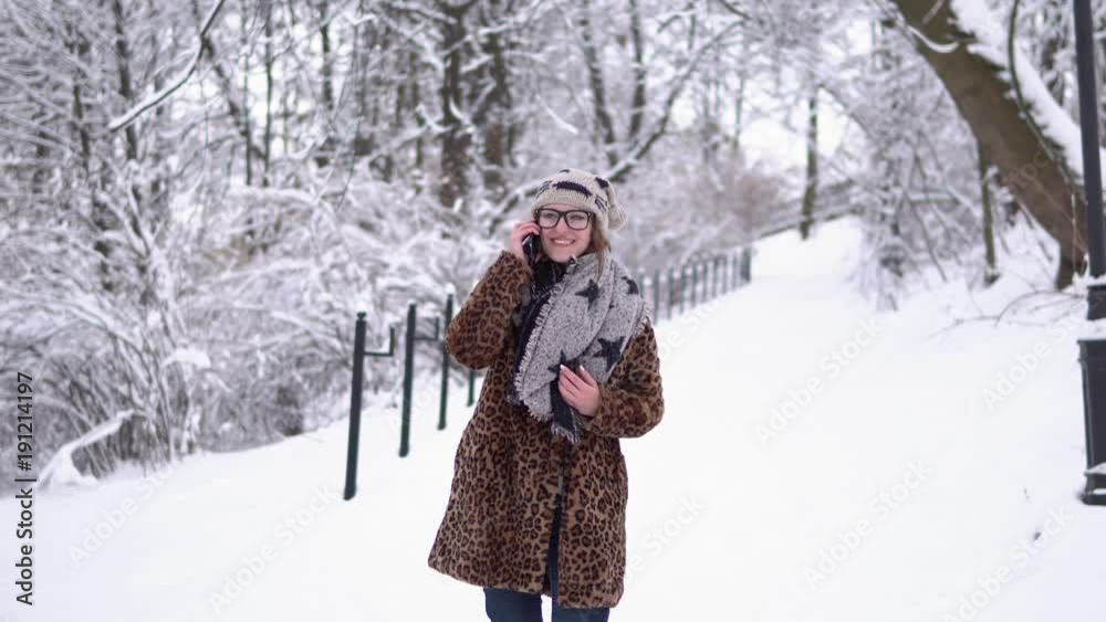 Attractive girl wears glasses talking by smartphone in winter snowy park Attractive girl wears glasses talking by smartphone in winter snowy park