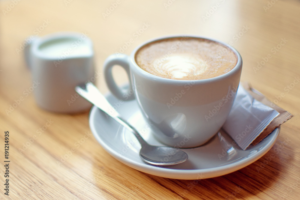 White cup of coffee with milk and sugar on the wooden table White cup of coffee with milk and sugar on the wooden table