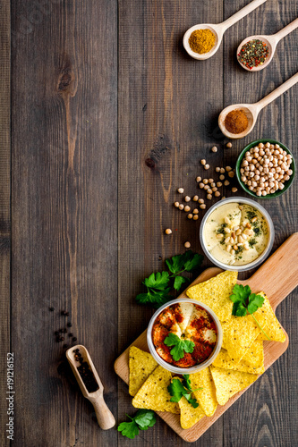 Serve hummus. Bowl with dish near pieces of crispbread on dark wooden background top view copy space