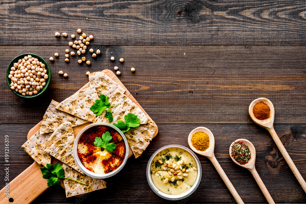 Serve hummus. Bowl with dish near pieces of crispbread on dark wooden background top view copy space Serve hummus. Bowl with dish near pieces of crispbread on dark wooden background top view copy space