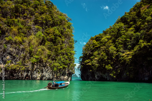 The boat floats between the rocks overgrown with tropical forest.