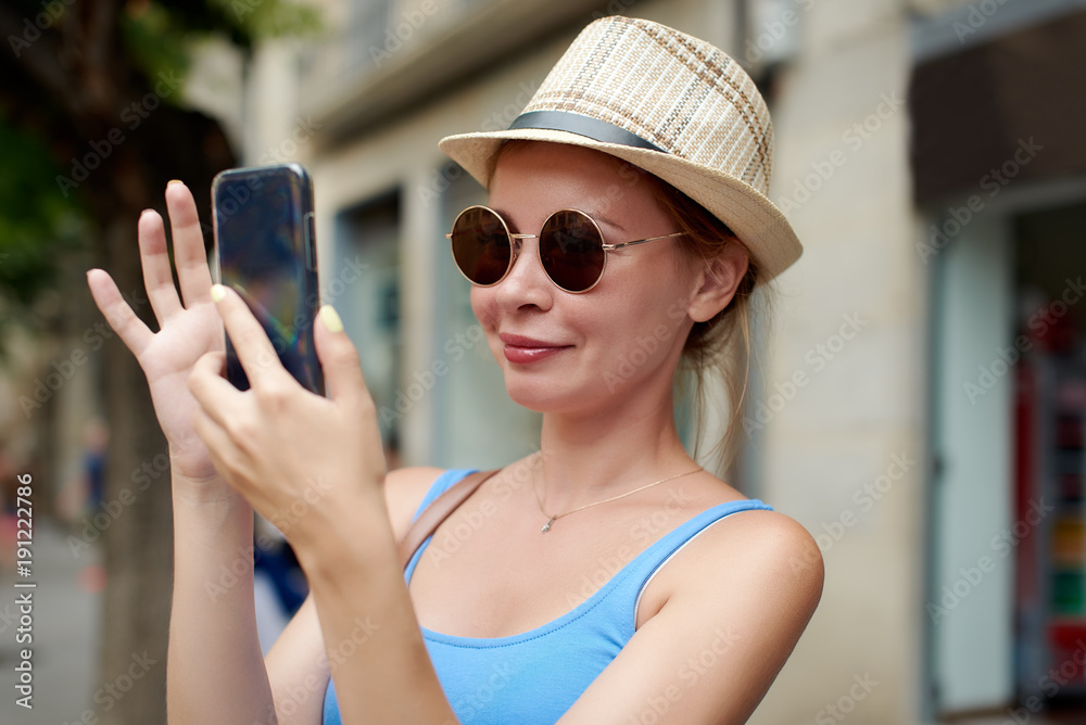 Smiling Caucasian female traveler is using mobile phone in a street. Smiling Caucasian female traveler is using mobile phone in a street.