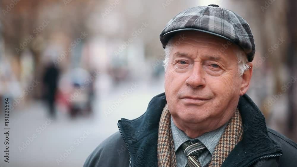 An impressive closeup of a wise man dressed in a black zipup coat and a woollen flat cap. He stands and thinks on a park alley in autumn. An impressive closeup of a wise man dressed in a black zipup coat and a woollen flat cap. He stands and thinks on a park alley in autumn.
