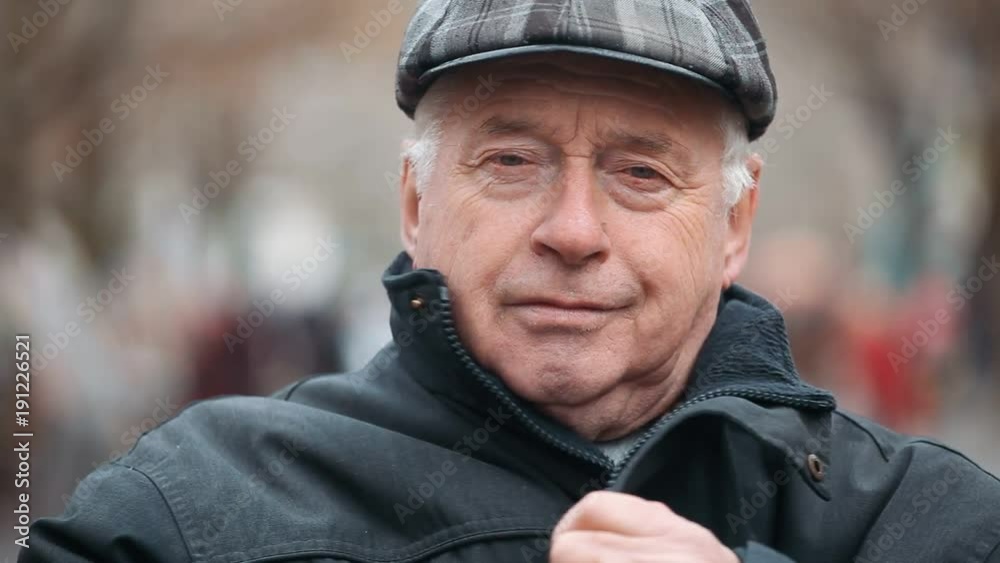 A splendid view of a senior man dressed in a black zipup coat and a woollen flat cap. He stands on a nice park alley and smiles in autumn. A splendid view of a senior man dressed in a black zipup coat and a woollen flat cap. He stands on a nice park alley and smiles in autumn.