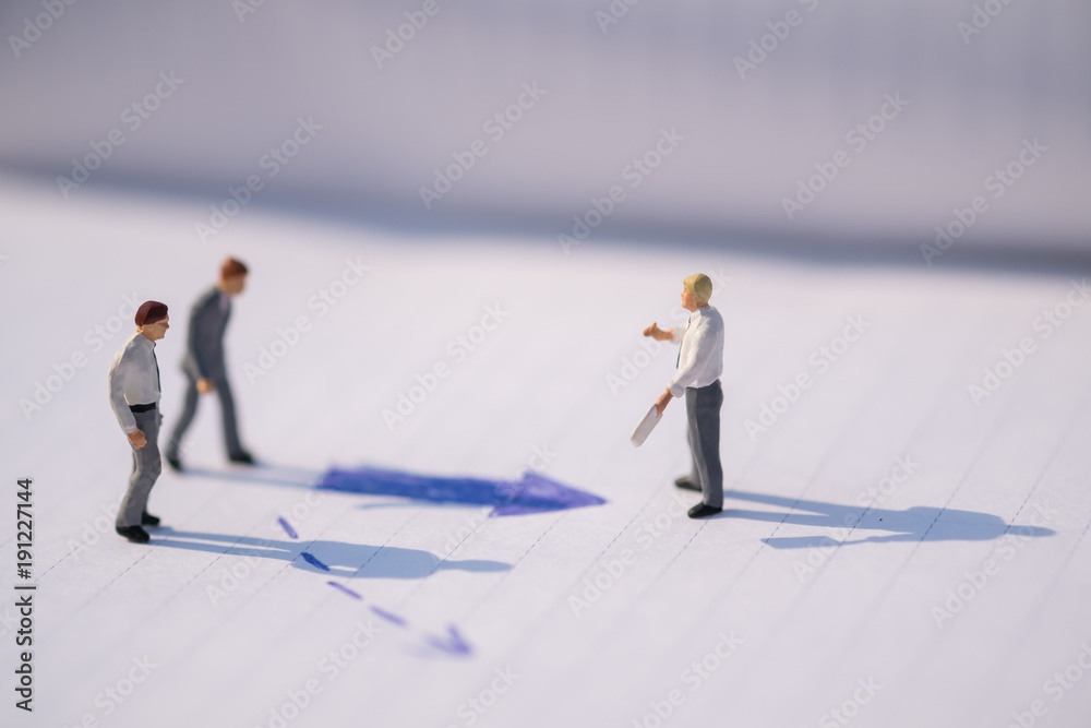 Business Direction concept. Group of businessman miniature figures standing, walking and standing on notebook with arrow signs under sunlight Business Direction concept. Group of businessman miniature figures standing, walking and standing on notebook with arrow signs under sunlight