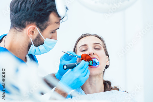Canvas-taulu Young woman during innovative oral treatment with cordless LED curing light mach