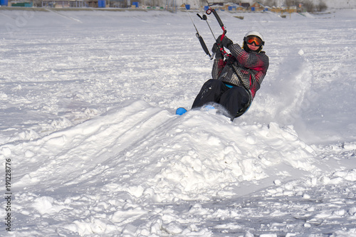 A male athlete engaged in snow kiting on the ice of a large snowy lake. He goes skiing in the snow. Winter sunny frosty day.