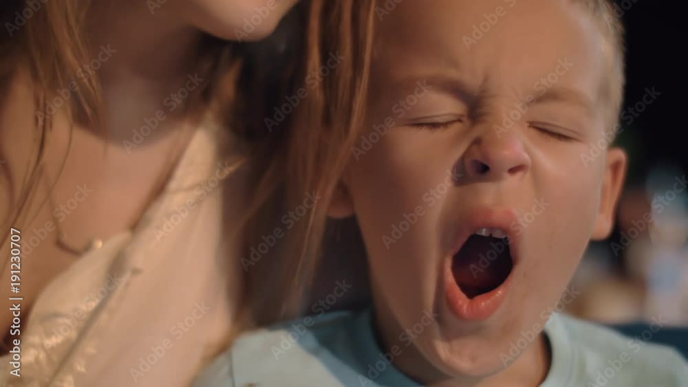 Boy with mum outdoor in the evening. Woman embracing and kissing beloved child who is tired and sleepy Boy with mum outdoor in the evening. Woman embracing and kissing beloved child who is tired and sleepy