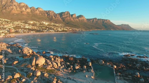 Drone shot from above of Camps Bay, Cape Town in South Africa at sunset with ocean, tide pool and mountains.