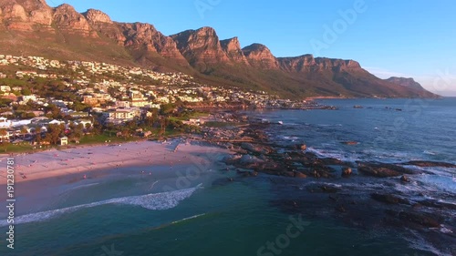 Aerial view of Camps Bay, Cape Town in South Africa at sunset with the ocean, beach, tourists and stunning mountains.