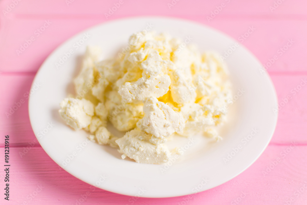 Cottage cheese on a white plate on a pink wooden background.