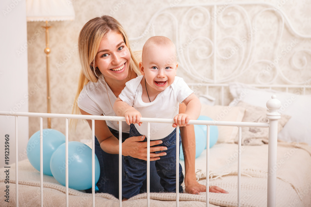 Young beautiful happy mother with baby on bed playing having fun and looking at camera. Mother's day. Happy mother with her son. Close-up Young beautiful happy mother with baby on bed playing having fun and looking at camera. Mother's day. Happy mother with her son. Close-up