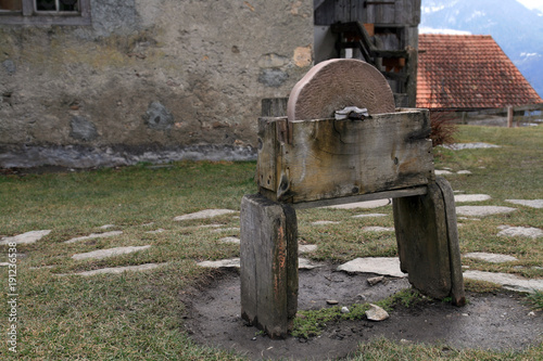 Old grinding machine. In the courtyard in front of the wall is an old stone grinding machine on the wooden bench. photo