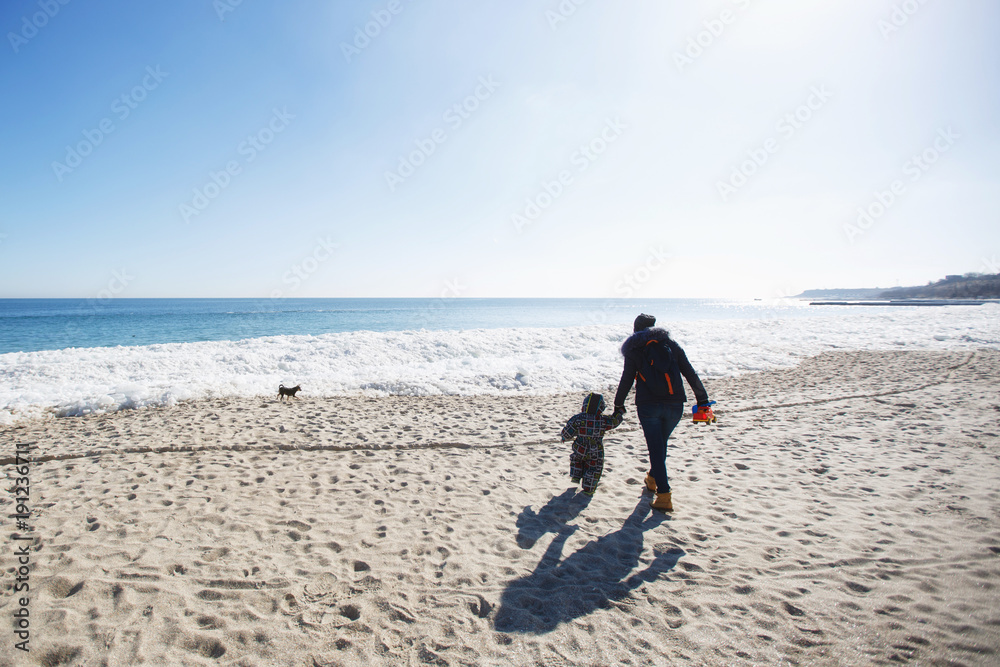 Woman play look at sea snow beach with little cute child baby boy in overalls with toy car, shovel. Mother, kid son fun on winter day. Family holiday 15 of may love parents children concept. Back view