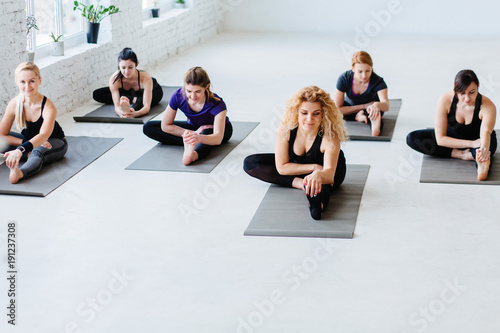 Group of happy young female sitting and stretching legs in yoga studio with white interior. Teamwork  good mood and healthy lifestyle concept.