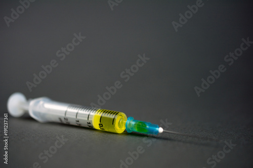 syringe with a yellow drug lies on a gray dark background, the concept of drug addiction, treatment of serious diseases. selective focus, close-up, copy-space