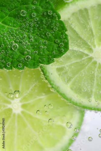 The slices of lime and peppermint leaves in soda water. Mojito close up. 