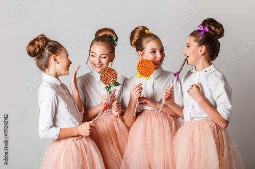 Beautiful teenage girls in pink tutu or tulle skirts with colorful lollipos in studio on white background