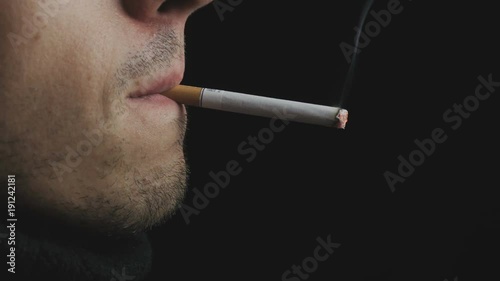 Close up of a brutal man smoking a cigarette at black background.