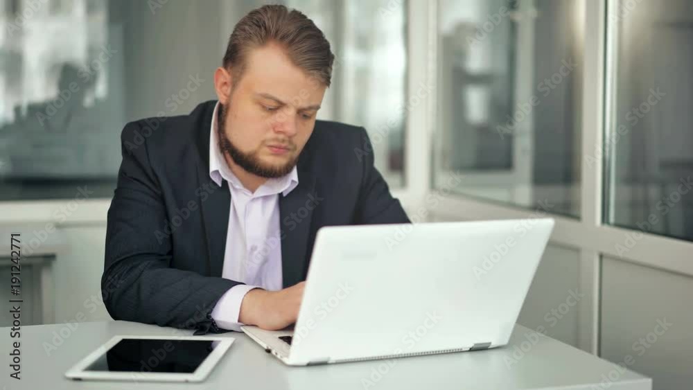 Young businessman working in office, sitting at desk, looking at laptop computer screen Young businessman working in office, sitting at desk, looking at laptop computer screen