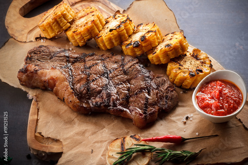 juicy steak on the grill With rosemary, garlic, chili and corn on the grill and bread on the wooden board