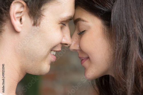 Romantic happy couple face to face close up portrait, smiling man and woman in love getting closer for first kiss, sensual sincere lovers touching noses with eyes closed, enjoying intimacy tenderness