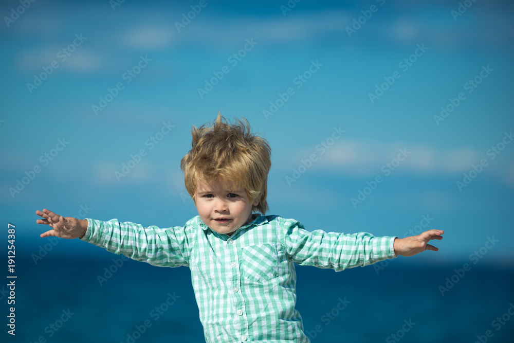 Airplane and child pilot. Little boy makes flying, blue sea and sky background. Child playing at sea shore waving his hands. All shades of blue and gentle skin color on photo with funny fly blond kid Airplane and child pilot. Little boy makes flying, blue sea and sky background. Child playing at sea shore waving his hands. All shades of blue and gentle skin color on photo with funny fly blond kid