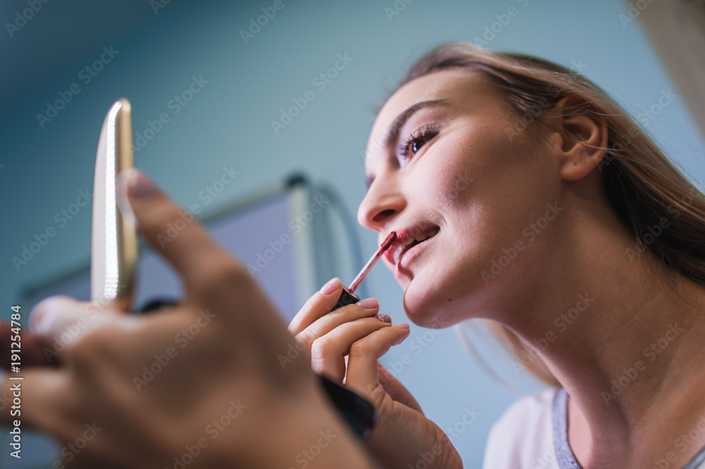 Young woman applying lipstick looking at mirror Young woman applying lipstick looking at mirror