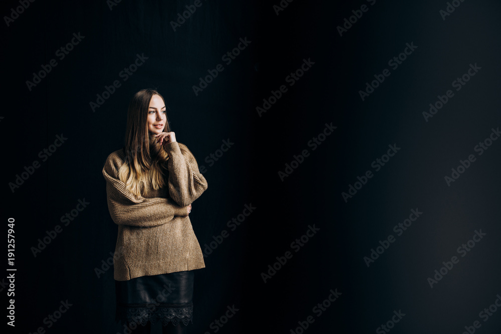 Portrait of a cute smiling girl with long hair who stands on a black background and looks out the window Portrait of a cute smiling girl with long hair who stands on a black background and looks out the window