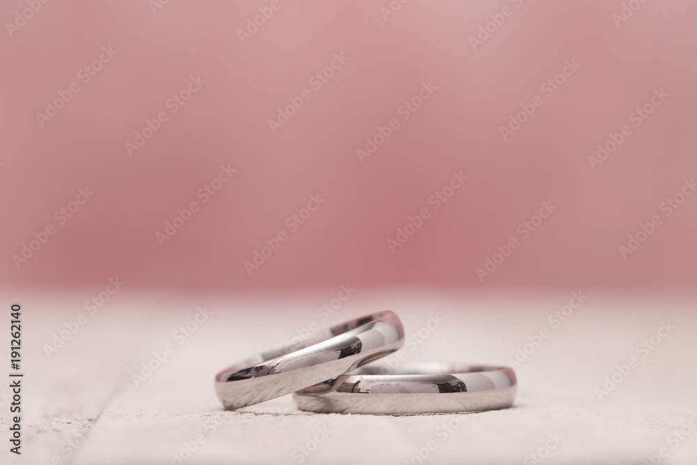 Macro View of Wedding Rings on a Wooden Table with Pink Background Macro View of Wedding Rings on a Wooden Table with Pink Background