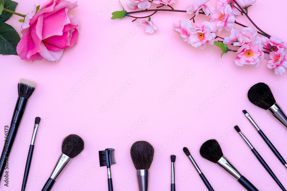 Set of makeup brushes, decorative cosmetics and flowers on pink colored composed background. Top view point, flat lay, space for text Set of makeup brushes, decorative cosmetics and flowers on pink colored composed background. Top view point, flat lay, space for text