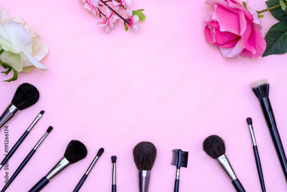 Set of makeup brushes, decorative cosmetics and flowers on pink colored composed background. Top view point, flat lay, space for text Set of makeup brushes, decorative cosmetics and flowers on pink colored composed background. Top view point, flat lay, space for text