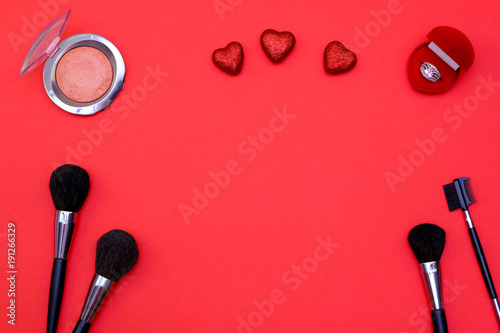 Set of make-up brushes, powder, ring and hearts on red colored composed background. Top view point, flat lay, space for text. Concept for valentines day