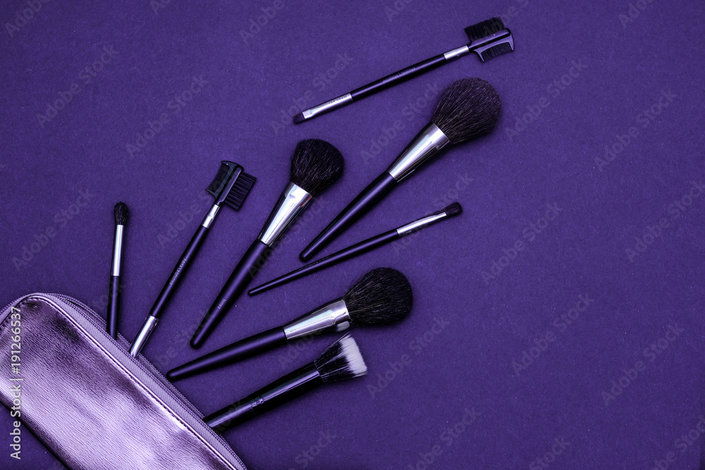 Set of makeup brushes with cosmetics bag on dark purple colored composed background. Top view point, flat lay Set of makeup brushes with cosmetics bag on dark purple colored composed background. Top view point, flat lay