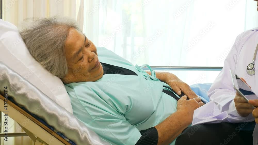 Yound Asian Doctor showing senior ethnic female patient care plan recorded on wireless tablet Yound Asian Doctor showing senior ethnic female patient care plan recorded on wireless tablet