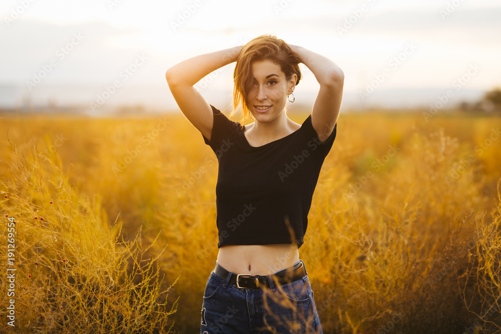 Young beautiful girl in the field. She wears a black T-shirt and jeans. Yellow background. Young beautiful girl in the field. She wears a black T-shirt and jeans. Yellow background.