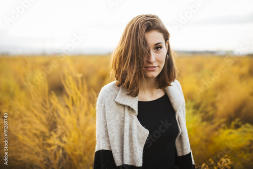 Young beautiful girl in the field. She wears a sweater and jeans. Yellow background.