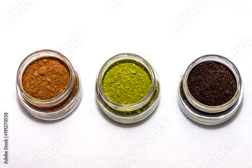 Cocoa powder, matcha tea powder, and ground coffee in little jars white background overhead photo