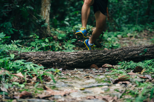 Athletic runner jumping cross tree trunk on tropical forest trail