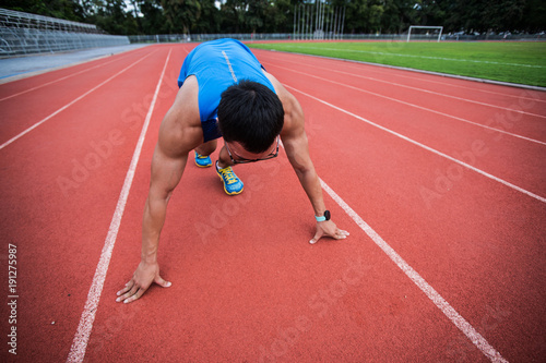 Attractive young man stretching on the track before running, copy space